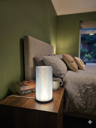 Moderne Tischlampe neben einem Bett mit grüner Wand und Kissen, Bücher und Tasse sichtbar.